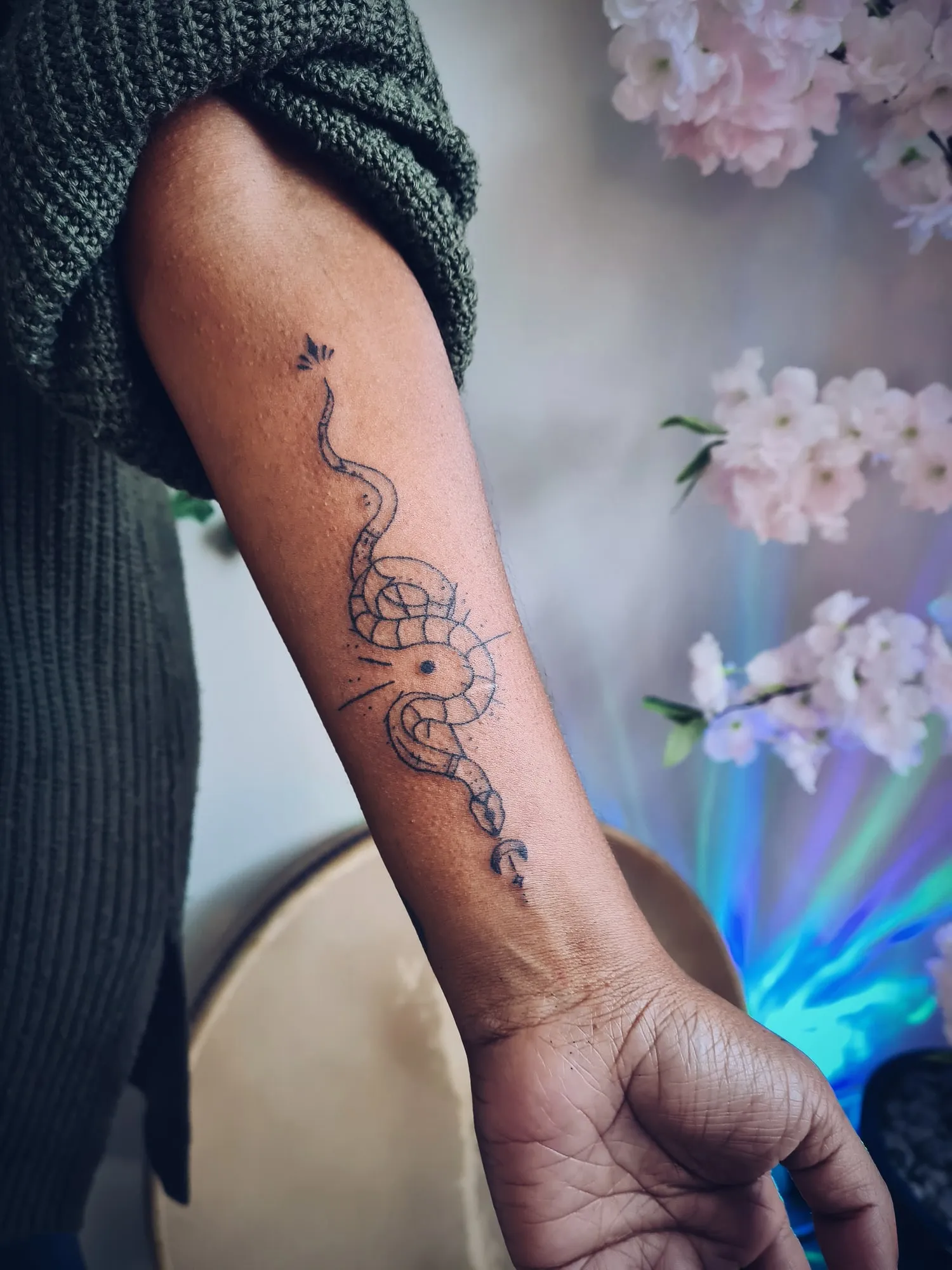 Tattoo van een slang rond een zon en maan op de onderarm