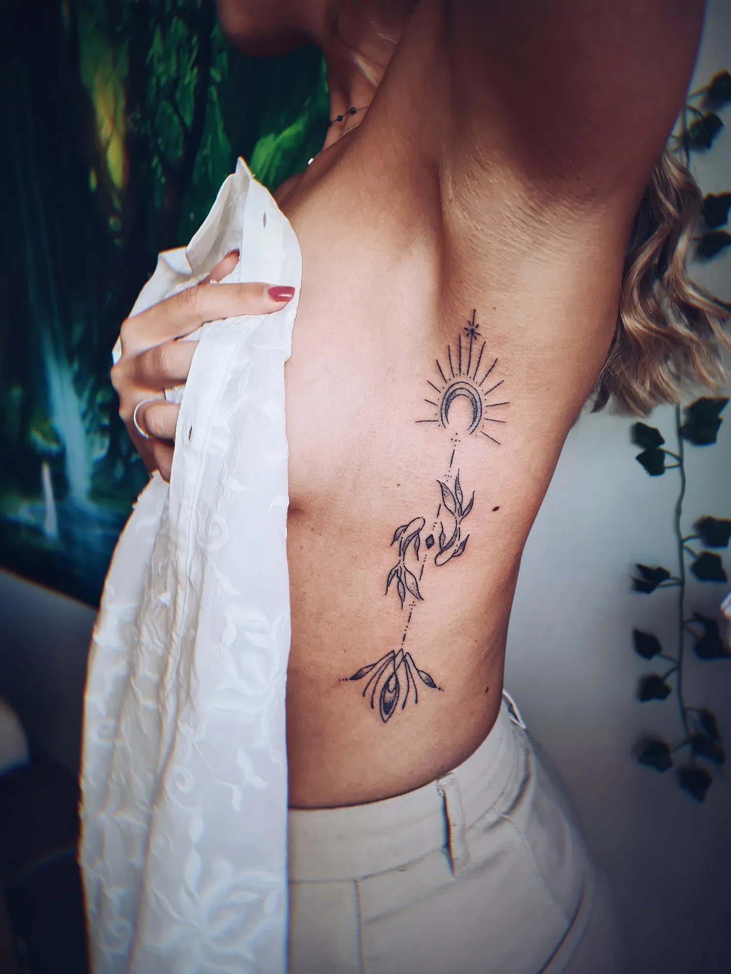 Tattoo van een zon met een plant op de ribben